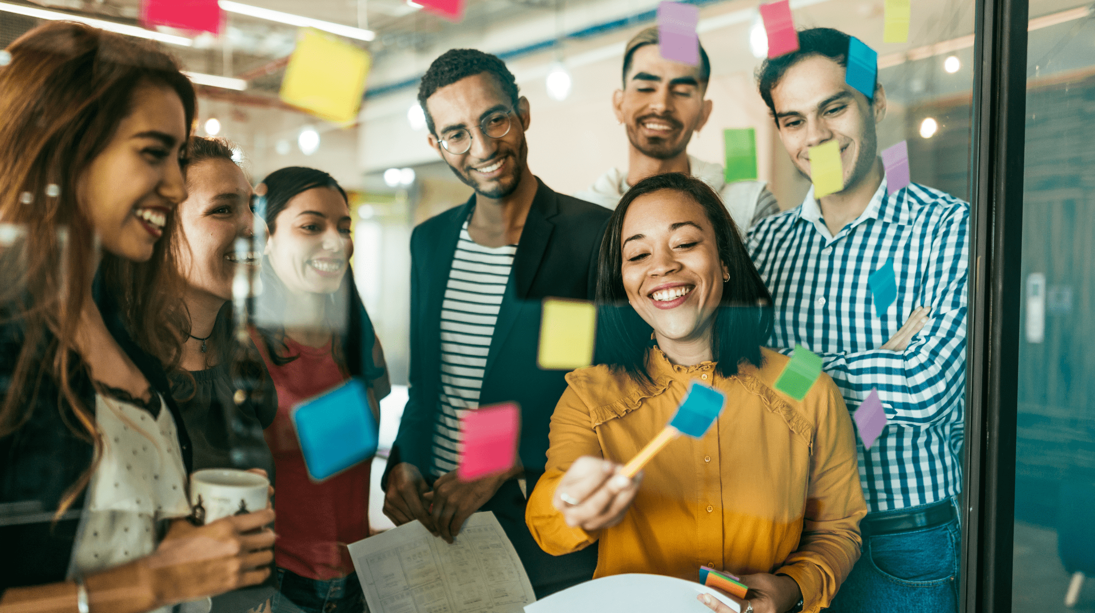 A group of smiling employees from the Customer Experience department analyzes colorful sticky notes 