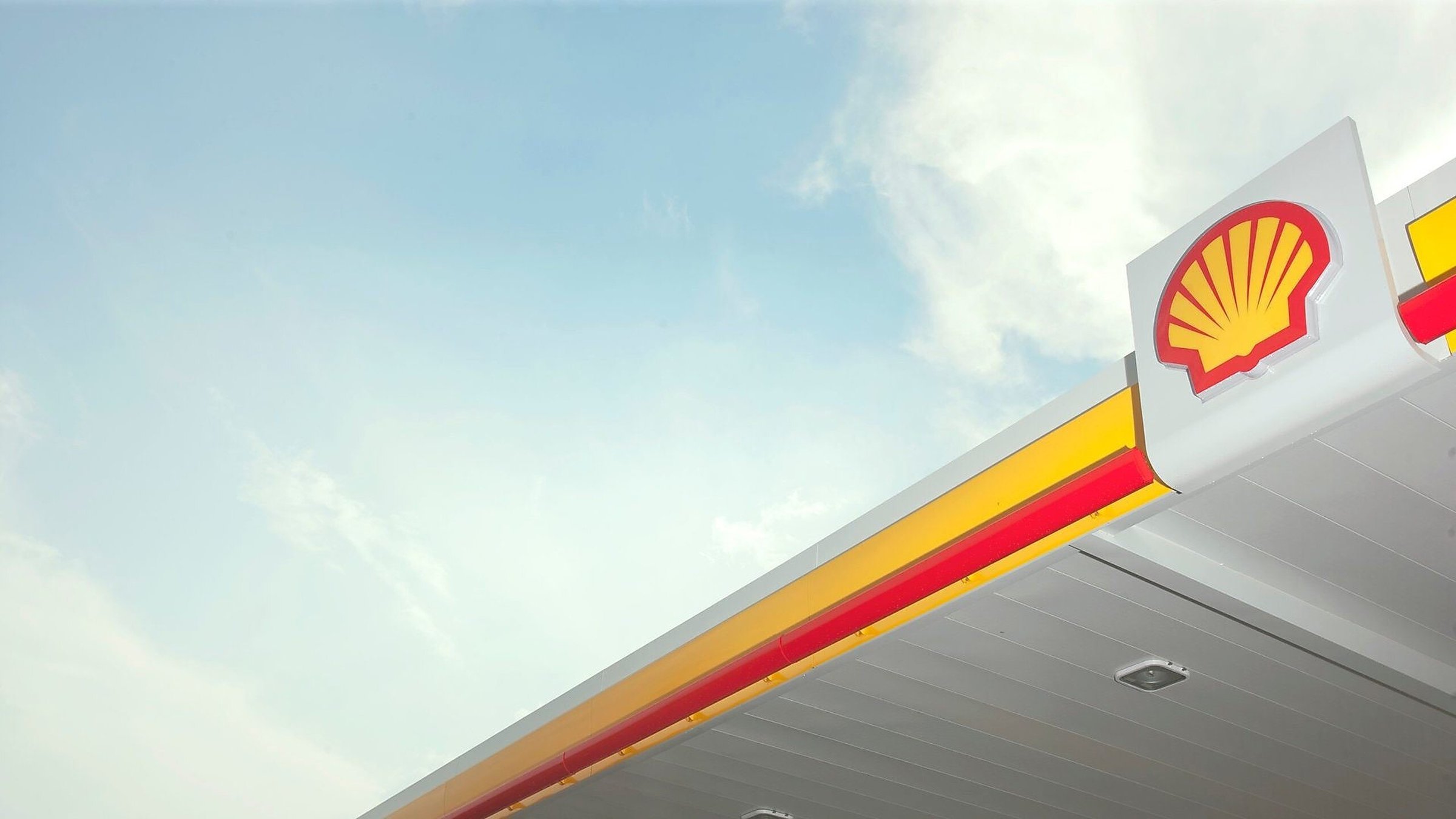 Shell gas station canopy with iconic yellow and red logo against a clear blue sky.