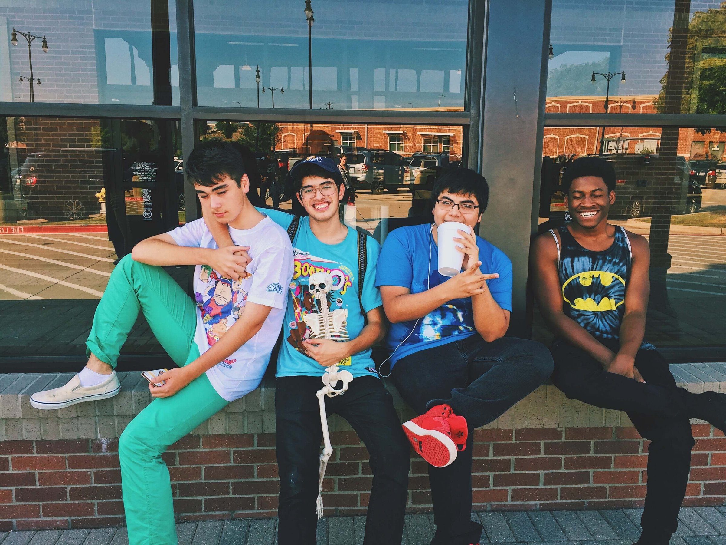 A group of four teenagers sit together on a wall and fool around. 