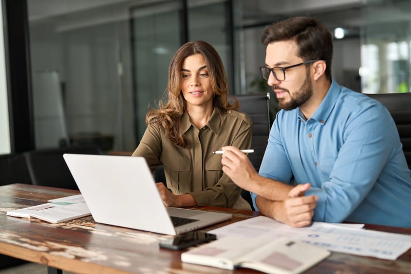 Female manager discussing business strategy with young colleague while reviewing data on laptop in office